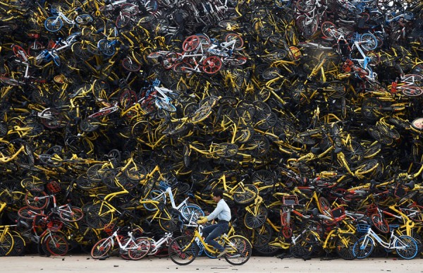 Worker rides a shared bicycle past piled-up shared bikes at a vacant lot in Xiamen